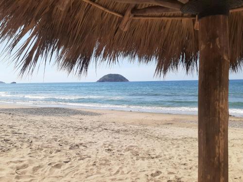 a straw umbrella on a beach with an island in the ocean at "Le Petit Oasis" Pool, AC and Beach 1 minute away in La Peñita de Jaltemba