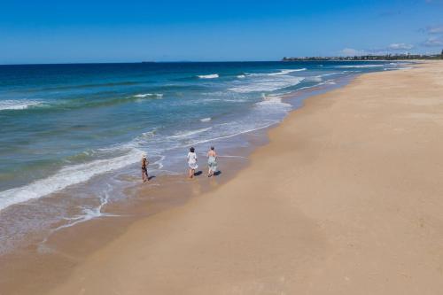 a group of three people walking on the beach at Pet Friendly House Opposite Bokarina Beach in Kawana Waters