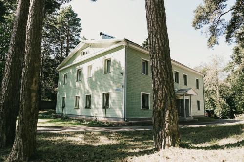 an old white house with trees in the foreground at Karja Apartment Narva-Jõesuu in Narva-Jõesuu