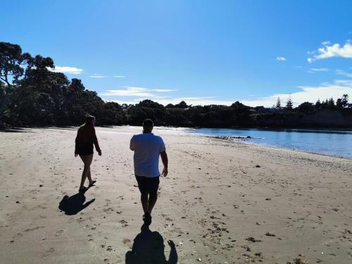 a man and woman walking on the beach at Tuia Retreat in Whangaparaoa
