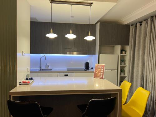 a kitchen with a island with yellow chairs and lights at Paxsafe Sydney Hyde Park Private Apartments in Sydney