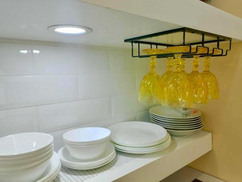 a pile of plates and bowls on a shelf in a kitchen at DaLei 2-330 Sleeps 8pax at Marina Spatial Condominium in Dumaguete City in Dumaguete