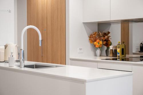 a white kitchen with a sink and a vase of flowers at Canberra Central,Modern 2BR Getaway, Parking,ANU in Braddon