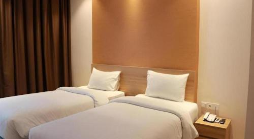 two beds in a hotel room with white sheets at Wing Hotel Kualanamu Airport in Medan