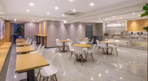 a restaurant with tables and white chairs and a kitchen at VX Hotel Wuxi Xinwu District Executive Center Wanda Plaza in Wuxi