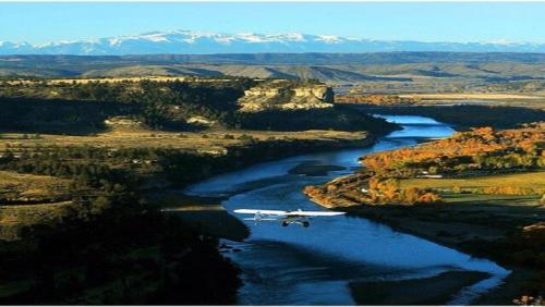 a plane flying over a river with mountains in the background at Yellowstone House of the Three Bears 2 Blocks to Downtown in Cody