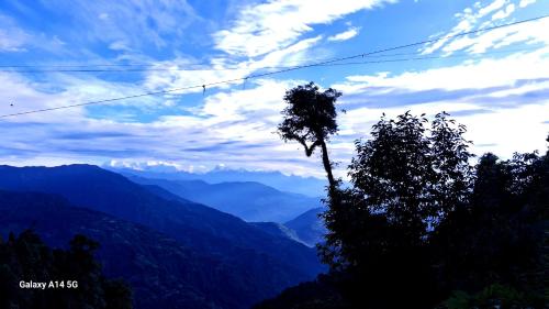 a tree in the foreground with mountains in the background at Lali Guras Homestay Simana in Darjeeling