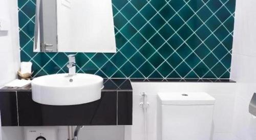 a bathroom with a white sink and a green tiled wall at Sans Hotel in Ratchaburi
