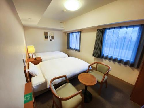 a hotel room with two beds and a table and chairs at Hotel Route-Inn Fukaya Ekimae in Fukaya