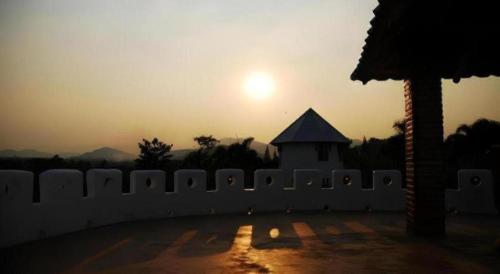 a sunset over a white fence with a building at Banrai Pornsawun in Ratchaburi
