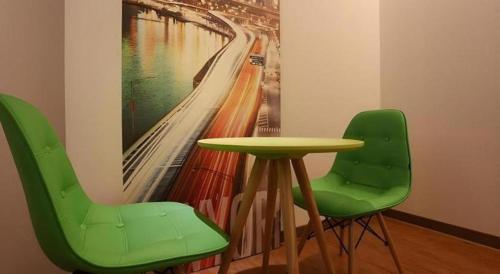 a table and two green chairs in a room with a painting at Java Hotel in Daejeon