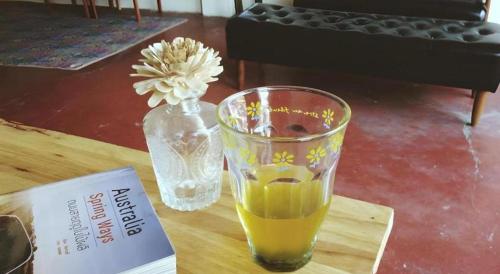 a glass of orange juice sitting on a table with a vase at Oldie and Sleepy Hostel in Udon Thani