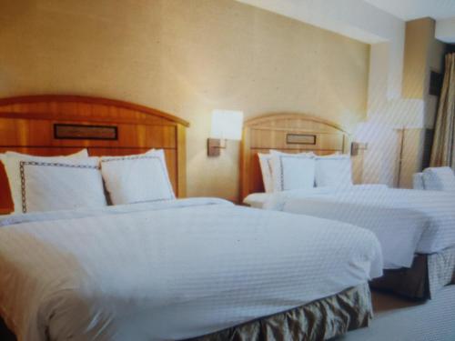 two beds in a hotel room with white sheets at Hotel Abhinandan in Manāli