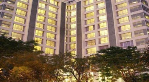 a tall building with many windows with trees in front at Grand Darmo Suite by AMITHYA in Surabaya