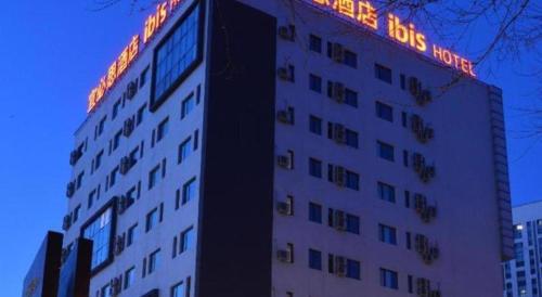 a tall white building with a neon sign on it at Ibis Harbin Normal University in Harbin