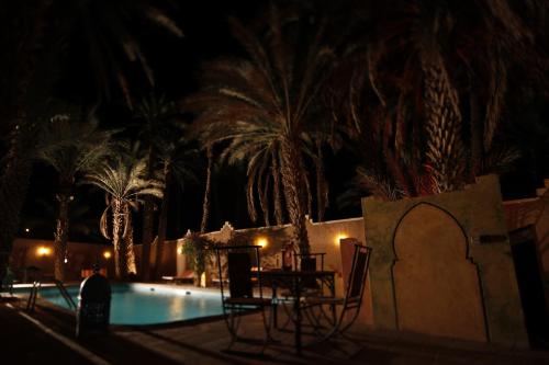 a pool at night with palm trees and a table and chairs at Fibule Du Draa Kasbah D'hôtes in Zagora