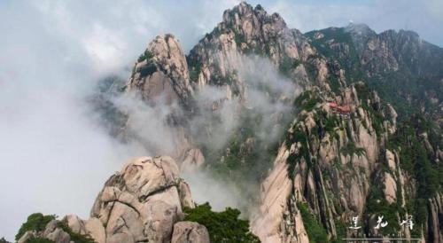a mountain covered in mist and clouds with trees in front at Huangshan Yupinglou Hotel in Huangshan