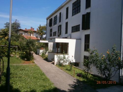 a white building with a sidewalk next to a yard at Apartman Lovran in Lovran
