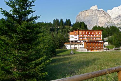 a building in a field next to a mountain at Hotel Meisules in Selva di Val Gardena