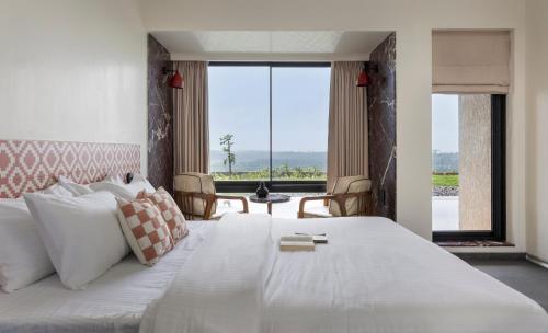 a bedroom with a large white bed with a large window at Scarlatta in Ghoti Budrukh