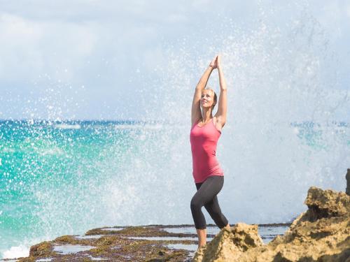 a woman doing yoga on the rocks by the ocean at Natura Cabana Boutique Hotel & SPA by Mint in Cabarete