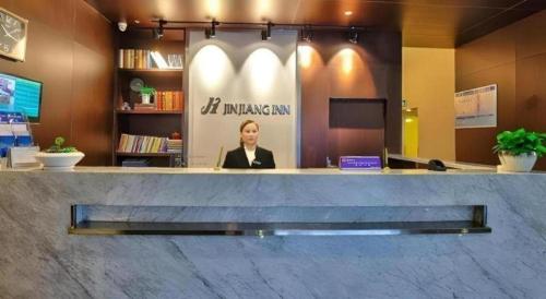 a woman sitting at a counter in a lobby at Jinjiang Inn Style Xiangshan Bus Station in Xiangshan
