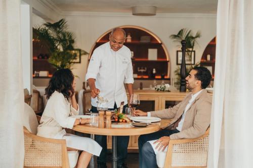 a group of people sitting around a table with a waiter at La Maison 20 Degrés Sud - Relais & Châteaux in Grand Baie