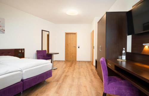 a bedroom with a bed and a desk with purple chairs at ates Hotel Lampertheim by AURUM in Lampertheim
