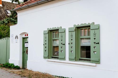 a white building with green windows and a fence at Kiskovász Pajta & Inn in Nagytevel