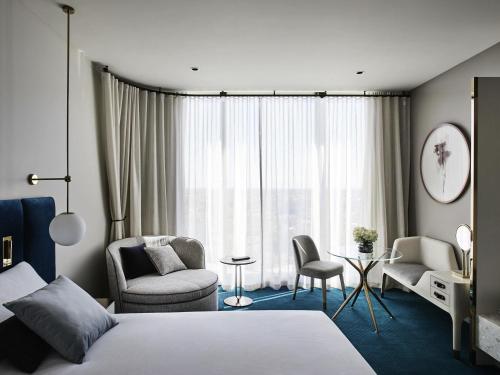 a hotel room with a bed and chairs and a window at Hotel Chadstone Melbourne MGallery Collection in Chadstone