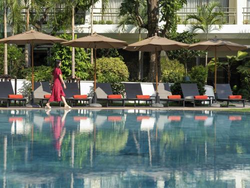 a woman walking next to a swimming pool at Mövenpick Hotel Bangkok Ploenchit BDMS in Bangkok