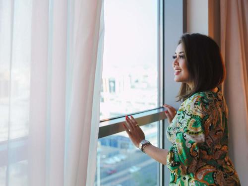 ジッダにあるAdagio Jeddah City Centerの窓の外を見ている女性