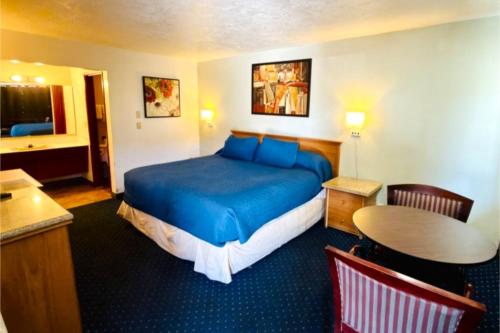 a hotel room with a blue bed and a table at Beaverton Budget Inn in Beaverton