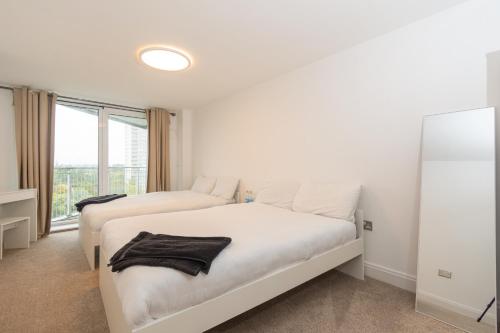 a white bedroom with two beds and a window at Spacious Shared Apartment by the Thames in Brentford