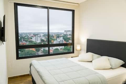 a bedroom with a white bed with a large window at Departamento de lujo en zona Carmelitas in Asuncion