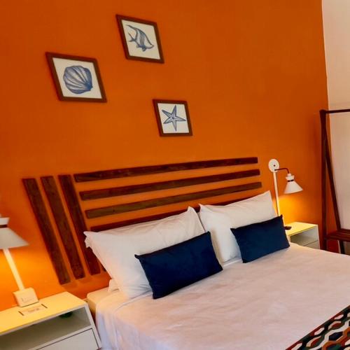 a bedroom with an orange wall with a bed with blue pillows at Pousada Villa Egregora in Itacimirim