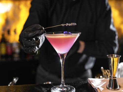 a person is stirring a pink drink in a martini glass at BERDS Hotel Chisinau - MGallery Collection in Chişinău