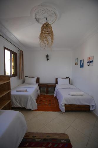 a white room with two beds and a fan at Onda Surf in Taghazout
