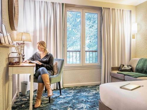a woman sitting at a desk in a hotel room at Hotel Novotel Domaine de Maffliers - Paris Val-d'Oise in Maffliers