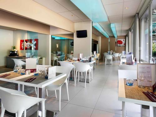 a restaurant with white tables and white chairs at Mercure Brive in Ussac