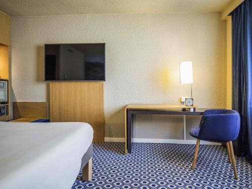 a hotel room with a desk and a bed and a bed and a room with at Novotel Orléans Chemins De Sologne Demeures De Campagne in Orléans