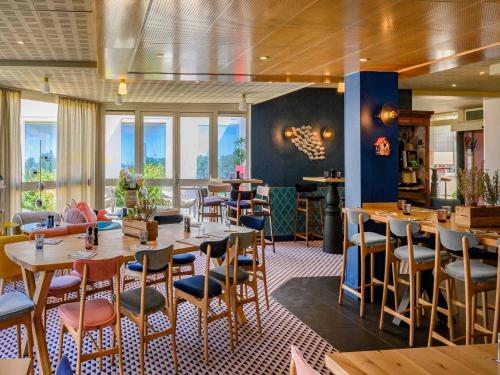 a restaurant with wooden tables and chairs and windows at Novotel Orléans Chemins De Sologne Demeures De Campagne in Orléans