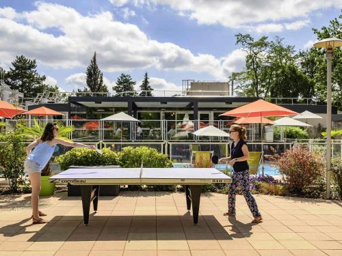 two women standing around a ping pong table at Novotel Orléans Chemins De Sologne Demeures De Campagne in Orléans