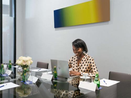 una mujer sentada en una mesa con una computadora portátil en Novotel Abidjan Plateau, en Abiyán