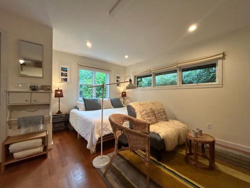 a bedroom with a bed and a chair and windows at Studio Cedar Guest Cottage in Duncan