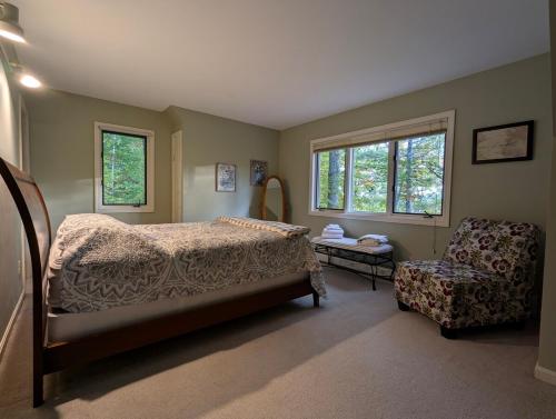 a bedroom with a bed and a chair and windows at Tranquil NH Lakehouse Escape in Moultonborough