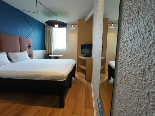 Un dormitorio con una cama y un escritorio con televisión. en ibis Lyon Est Bron, en Bron