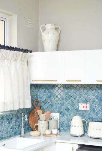 a kitchen with white cabinets and a blue tiled wall at The Loft Apartment in Gaborone in Gaborone
