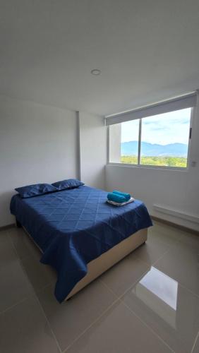 a bedroom with a bed with a blue comforter and a window at Relájate y Disfruta, Apartamento con Piscina, Tobogán y Vista Espectacular en Santa Fé de Antioquia in Santa Fe de Antioquia