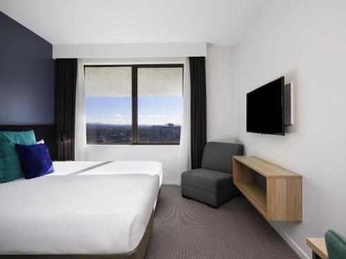 a hotel room with a bed and a tv and a chair at Mantra MacArthur Hotel in Canberra